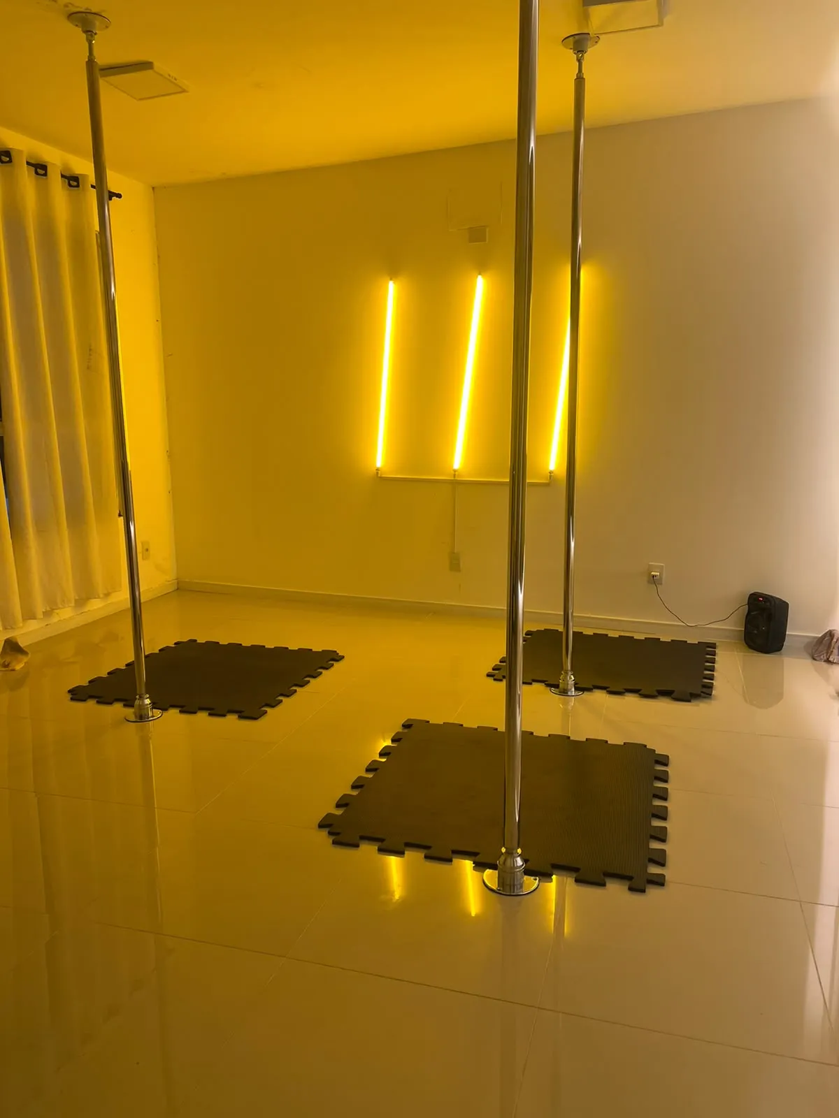 Sala do Evoá Pole Studio com barras de pole dance e neon amarelo na parede