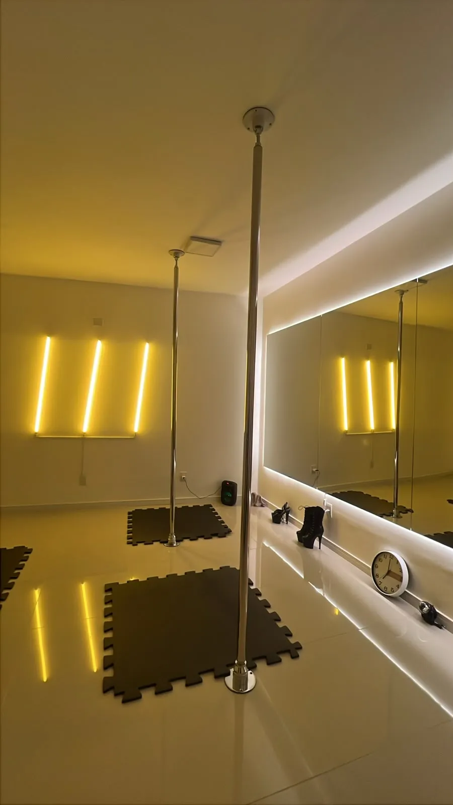 Sala de aula da Evoá com barras de pole, espelho iluminado e neon